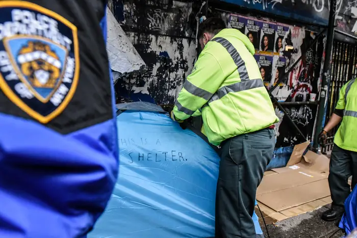 A blue tent with the words "this is a shelter" written on it is surrounded by NYPD officers.